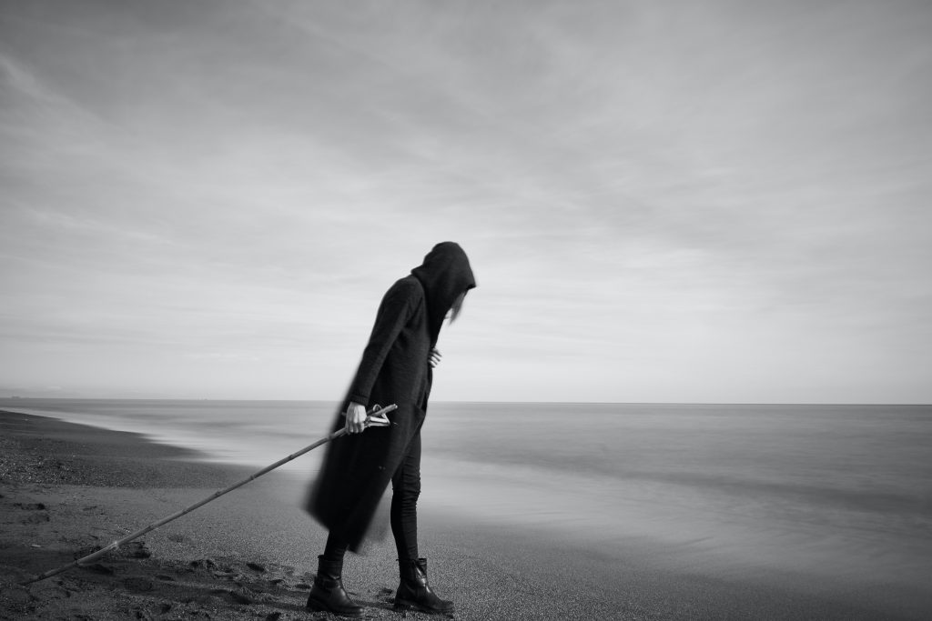 woman in black cloak with fishing pole standing in beach 2174618 scaled